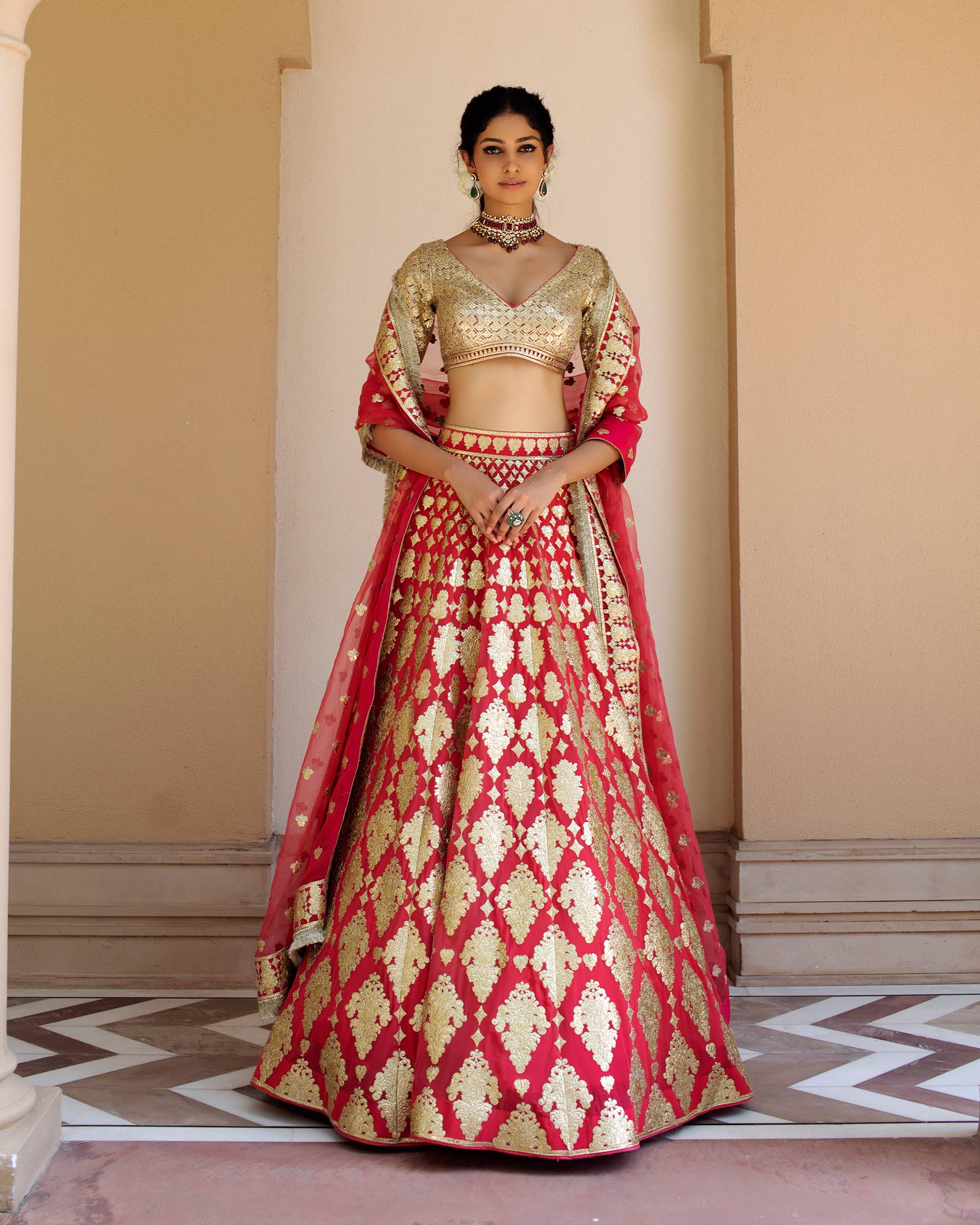 Photo of Bride twirling in red and gold lehenga with green jewellery